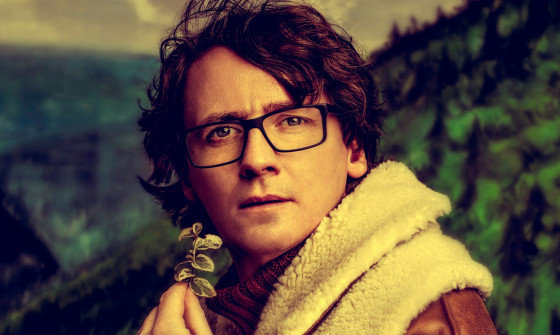 Ed Byrne in front of an image of a mountain, he's holding a leaf