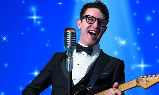 'Buddy Holly' stands smiling and singing as he plays a guitar in front of a wintery backdrop.