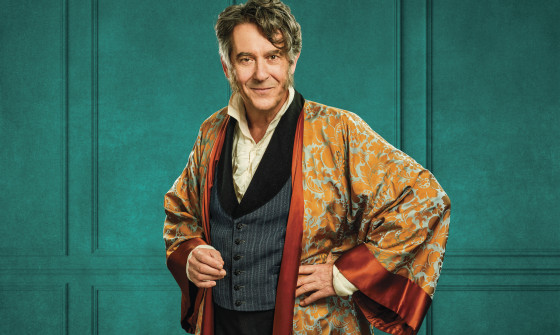 Adrian Lukis stands in a period gown and suit.