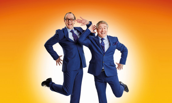 Ian Ashpitel and Jonty Stephens pose in front of an orange background.