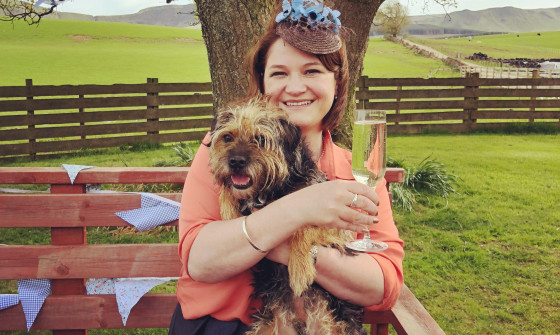 Gill Sims smiling with a dog on her lap and a drink in her hand