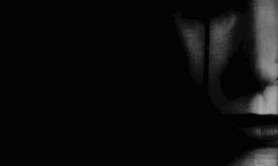 A veiled figure stands in darkness.
