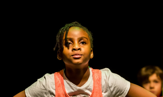 A young girl on stage looking out past the camera with her hands on her hips
