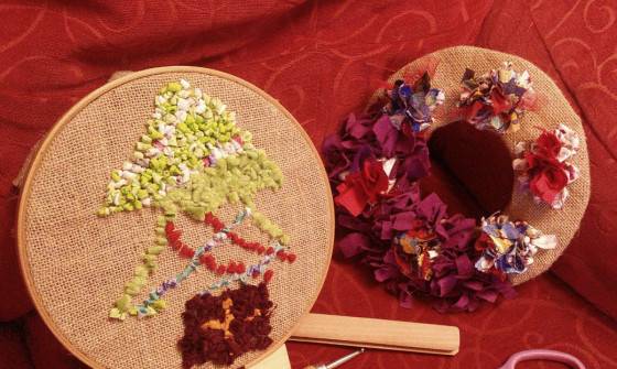 Two embroidery hoops sit on an armchair with scissors and a crafting tool. A Christmas tree is crafted onto one of the hoops.