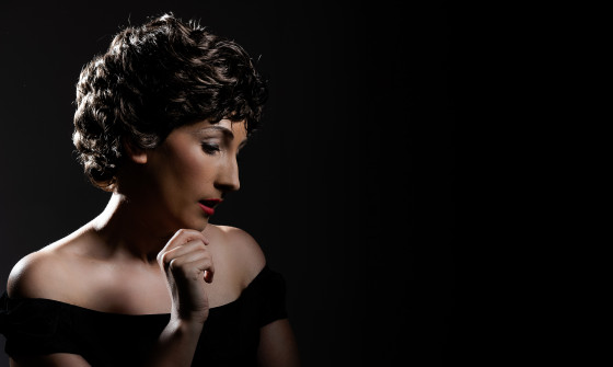 A tribute artist to Judy Garland sits in silhouette, looking down.