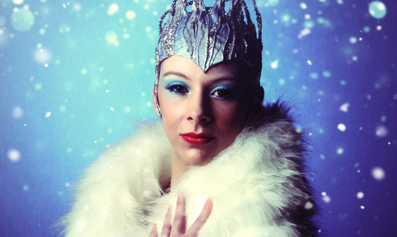The Snow Queen is facing the camera. She is wrapped in a fur coat and wears a crown