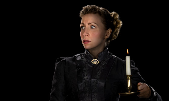 A lady in a black dress hold a lit candle in the dark