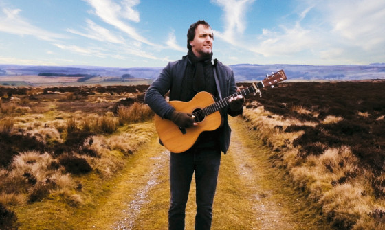 Jon Boden in a field playing guitar