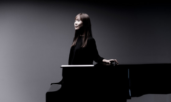 Yeol Eum Son stands next to a piano. Her hand is resting on top of it