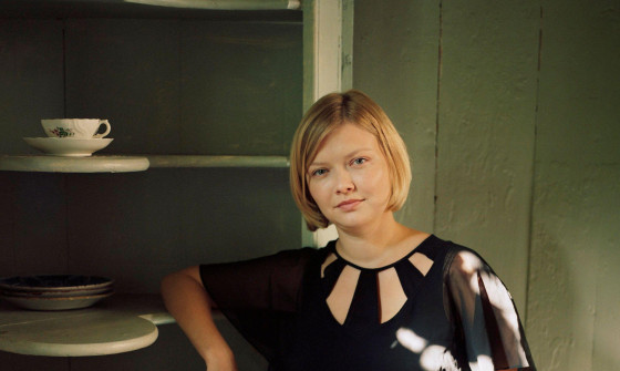 Alina Ibragimova is standing with her right arm resting against a shelf