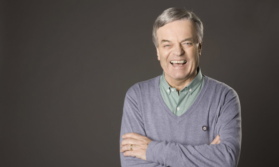 A close up of Tony Blackburn who laughs at the camera. His arms are crossed.