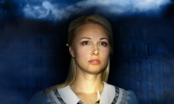 A blonde woman stands with a candle in darkness looking out past the camera. She is dressed in a pale blue dress with a detailed white collar.