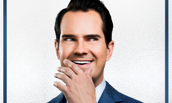 Jimmy Carr puts his hand to his face as he laughs.