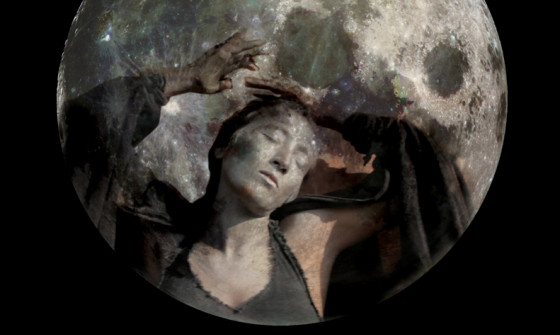 A woman in silver face paint sits inside the moon.