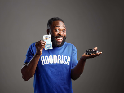 Kojo Anim holds a black cab toy in one hand and a £5 note in the other, grinning at the camera