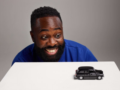Kojo Anim looks down at a miniature black cab model, grinning widely