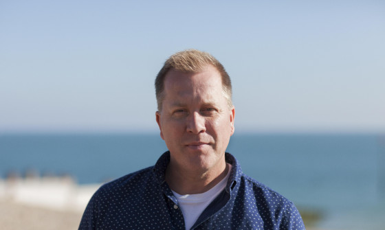 Tony Stockwell stands on a beach looking into the camera