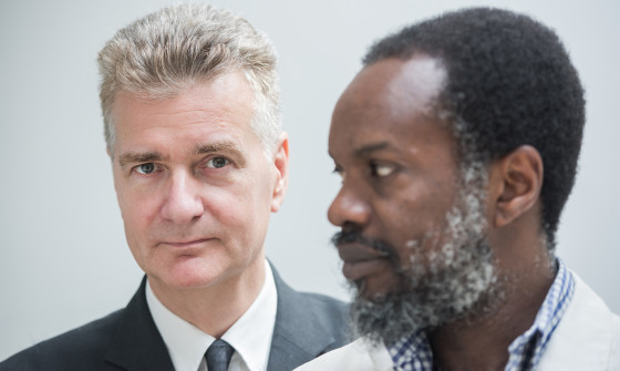 McAlmont & Webb stand in front of a white background, one in front of the other.
