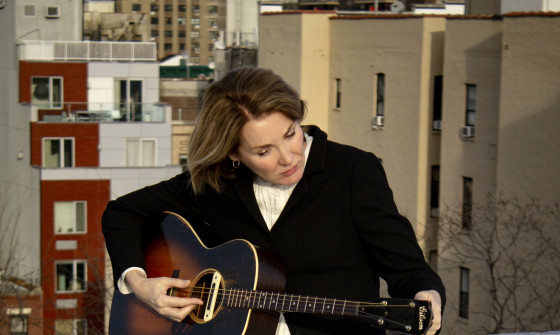 Diana Jones sits on a wall tuning an acoustic guitar