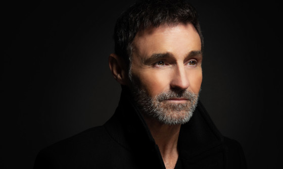 Marti Pellow dressed in black with a dark background, looking away from the camera